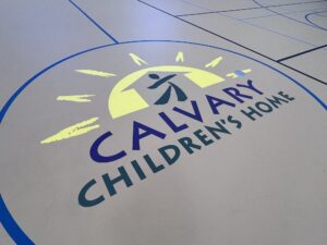 Calvary Children’s Home is a home for children in the Metro Atlanta, Located on a thirteen-acre campus in Powder Springs, Georgia. 1430 Lost Mountain Road, Powder Springs, GA 30127 MONOFLEX RUBBERIZED POURED FLOOR, Gym Floor Monoflex is seamless polyurethane, dual durometer, indoor sports flooring system. This system features a recycled, rubber-based mat and polyurethanes that are 100% free of mercury and heavy-metals creating a floor that’s as safe as it is durable. Our Monoflex surface provides ideal shock absorption, consistent playing characteristics, true ball rebound, durability and a high resistance to rolling loads. It is ideal for indoor basketball, volleyball, tennis, track, as a multi-sport court, or any other type of sport and recreational usage. Monoflex has excellent slip, abrasion and wear resistance and is also durable enough for multi-use events like meetings, church services and dances. The seamless surface is made up of three layers of poured urethane over a pre-fabricated and fully adhered rubber-based mat. You can add custom graphics, logos or mascots to this surface to complement your school or theme.